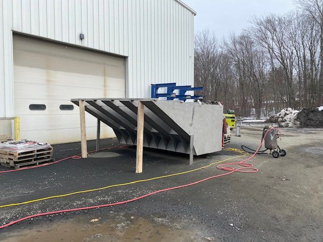 Industrial outdoor setting with a concrete ramp, a pallet of materials, and a portable air compressor hose system featuring positive customer reviews.
